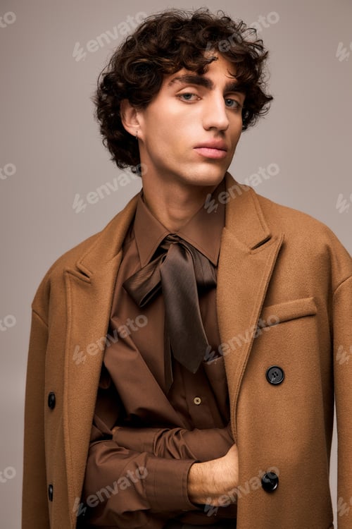Preview: Stylish young man exudes modern elegance with unique fashion choices in warm tones