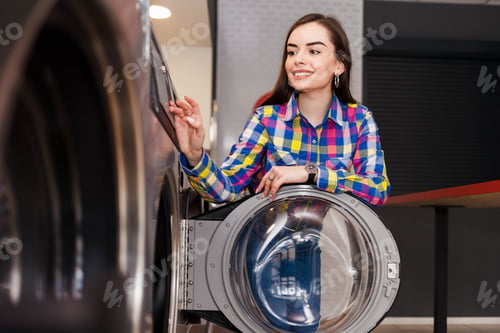 Preview: Woman leaned on the door of the washing machine at the self service launderette.