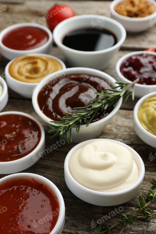 Preview: Different tasty sauces in bowls, rosemary and thyme on wooden table, closeup