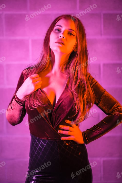 Preview: brown and black tight suit on a brick wall, posed at night illuminated with pink light
