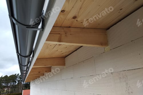 Preview: Building fasade under construction with unfinished wall and wooden roof boards with plastic gutter