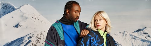 Preview: stylish multicultural couple in bold clothes with snowy mountain on backdrop, winter concept, banner