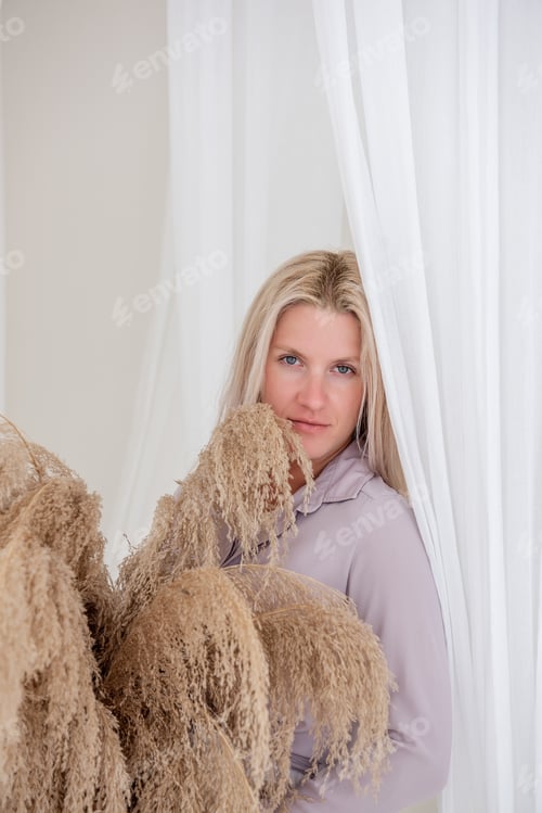 Preview: Young blonde woman lilac shirt holds in hands straw basket with pampas grass. Minimalist loft
