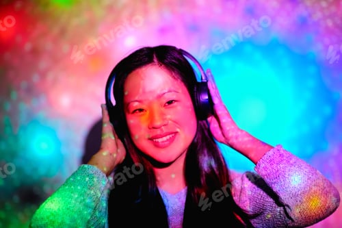 Preview: Happy Asian woman in headphones under bright illumination in stu