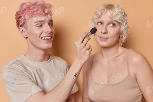 Preview: Happy freckled pink haired boyfriend uses professional cosmetic brush applies facial powder on