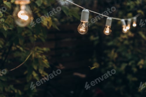 Preview: Beautiful night yellow light bulbs on the street. Lightbulb hanging at the dark summer night
