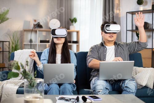 Preview: Asian couple sitting on couch with VR headset and laptops