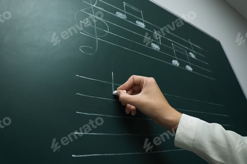 Preview: Teacher writing music notes with chalk on greenboard, closeup