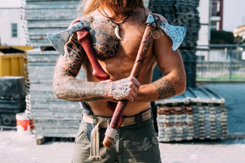 Preview: Tattooed man showing off handcrafted axes