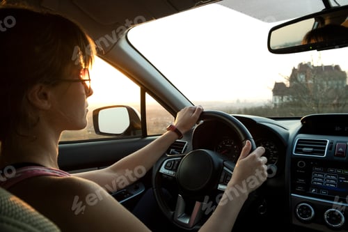 Preview: Close up view of a woman driver holding steering wheel driving a car at sunset