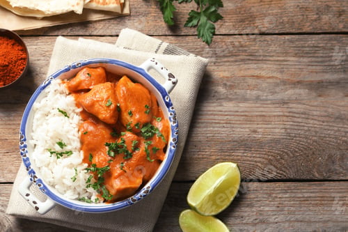Preview: Delicious butter chicken with rice served on wooden table, flat lay. Space for text