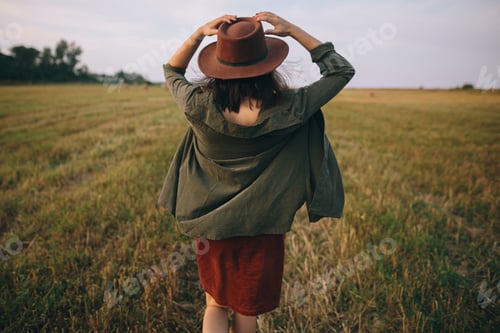 Preview: Beautiful carefree woman in hat walking in evening summer field. Relaxing in countryside. Happiness