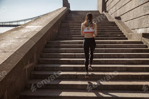 Preview: Sportive lady in modern tracksuit runs up stone stairs on city waterfront
