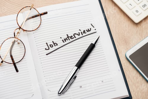 Preview: notebook with pen, glasses and job interview lettering on wooden table