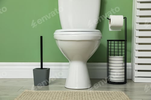 Preview: Ceramic toilet bowl, brush and paper near green wall indoors
