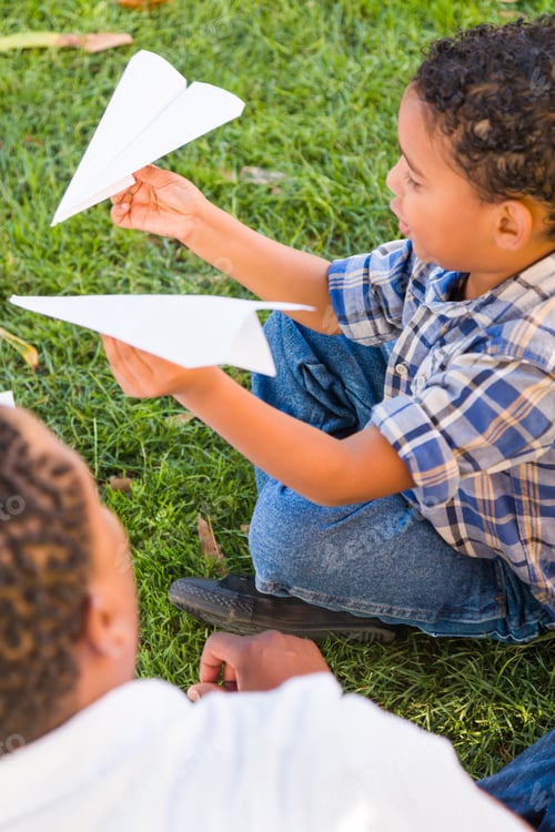 Preview: Happy African American Father and Mixed Race Son Playing with Paper Airplanes in the Park