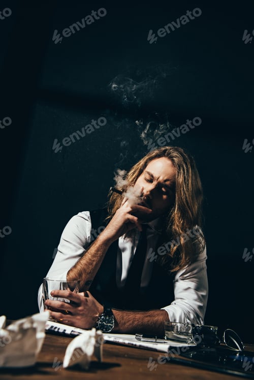 Preview: Handsome stylish young man drinking alcohol and smoking cigar while sitting at table