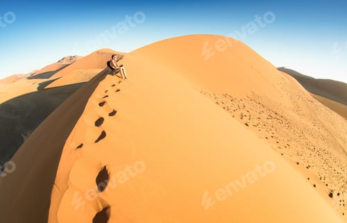 Preview: Lonely man sitting on sand at Dune 45 in Sossusvlei