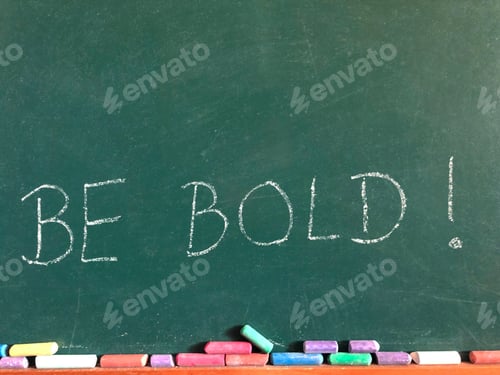 Preview: The words Be Bold! written on a chalkboard with coloured chalk sticks and copy space
