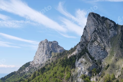 Preview: Swiss alps covered with forests and rocks near the French border under a blue cloudy sky