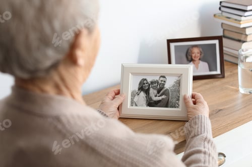 Preview: Elderly woman with framed family portrait at home