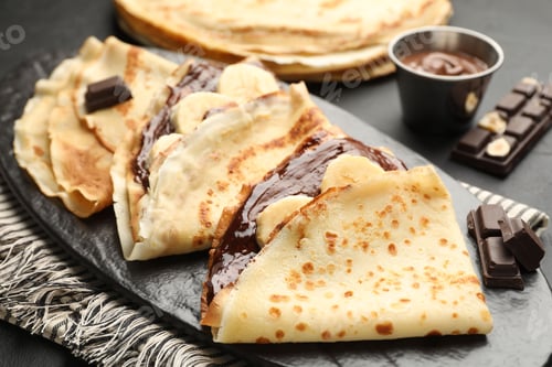Preview: Tasty crepes with chocolate butter and banana on black table, closeup