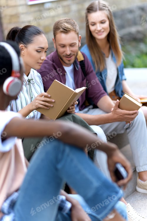 Preview: young multiethnic students studying and reading books while sitting outside university building