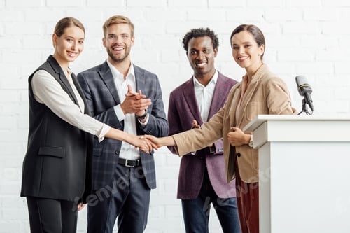 Preview: four multiethnic colleagues in formal wear talking and shaking hands in conference hall