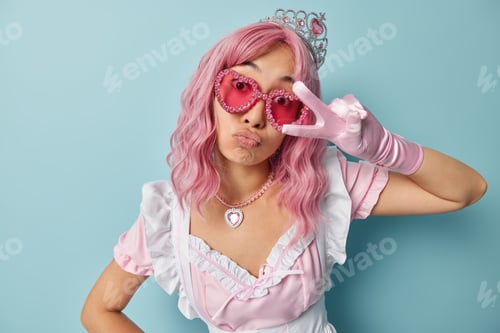Preview: Horizontal shot of pink haired housemaid makes peace gesture over eye pouts lips wears crown sunglas