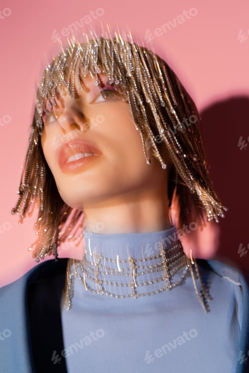 Preview: Long exposure of stylish model in jewelry headwear looking away on pink background
