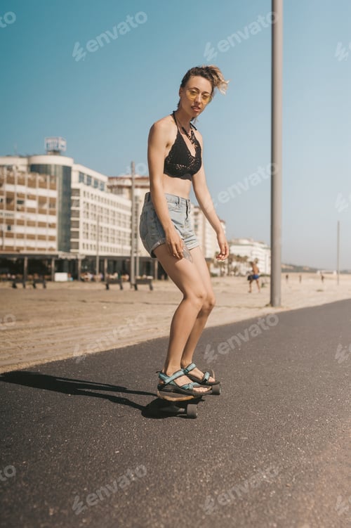 Preview: young woman in sunglasses skating on longboard on street in Portugal