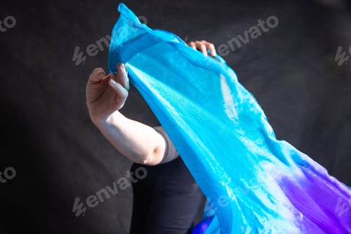 Preview: Young woman holding a blue scarf in her hand against a black background