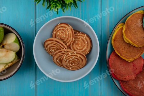 Preview: top view cookies in a bowl with multicolored pancakes on a plate on a turquoise background