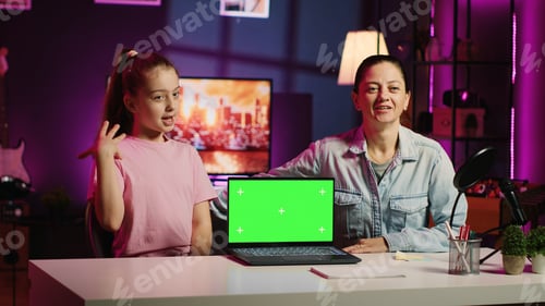 Preview: Daughter and mother in home studio film video together next to green screen laptop