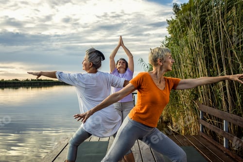 Preview: Group of senior woman doing yoga exercises by the lake.