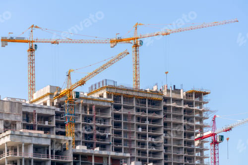 Preview: Low angle shot of cranes next to a buildings under construction against a blue sky