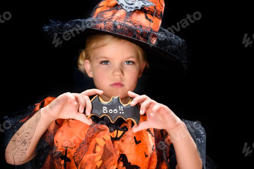 Preview: child in halloween costume of witch holding bat cookie, isolated on black