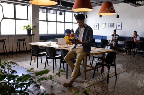 Preview: Biracial male creative sitting on desk using tablet in casual office