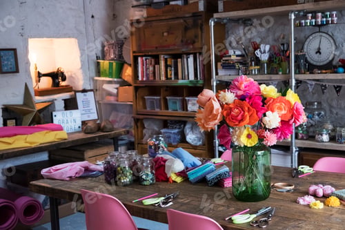 Preview: A bunch of colourful handcrafted fabric flowers in a vase on a table in a workshop.