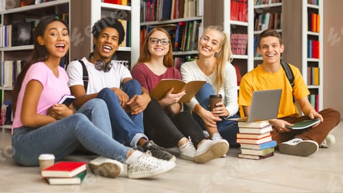 Preview: Group of diverse teenage classmates sitting on library floor