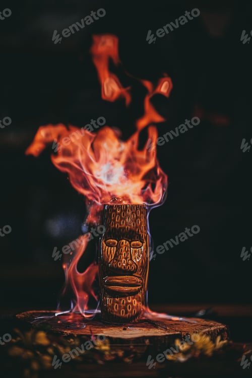 Preview: Vertical shot of a burning cocktail in a tiki cup on a wooden board.