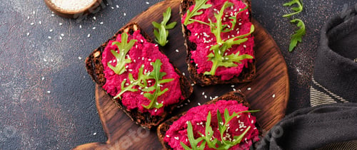 Preview: Bruschetta with beetroot hummus, arugula and sesame seeds on dark concrete background. Top view