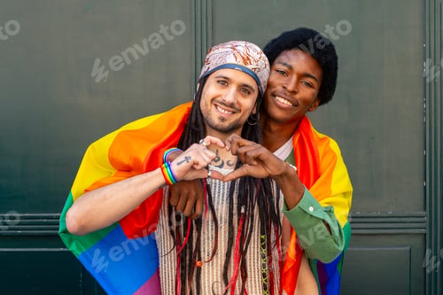 Preview: Happy gay couple making heart shape with hands wrapped in rainbow flag