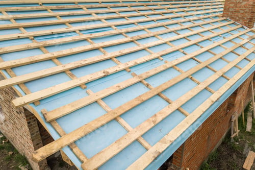 Preview: Aerial view of a brick house with wooden roof frame under construction.