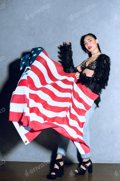 Preview: beautiful asian woman with american flag posing against concrete wall