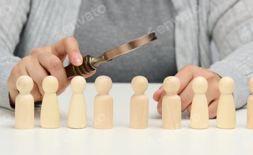 Preview: Figurines of men on a white table, a female hand holds a magnifying glass over one.