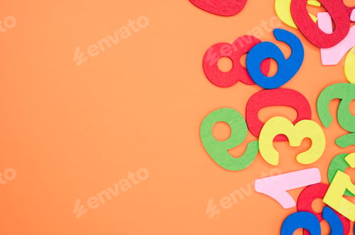 Preview: Flat lay of colorful wooden numbers scattered on an orange surface - space for text