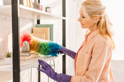 Preview: Senior woman in rubber gloves cleaning shelves with duster