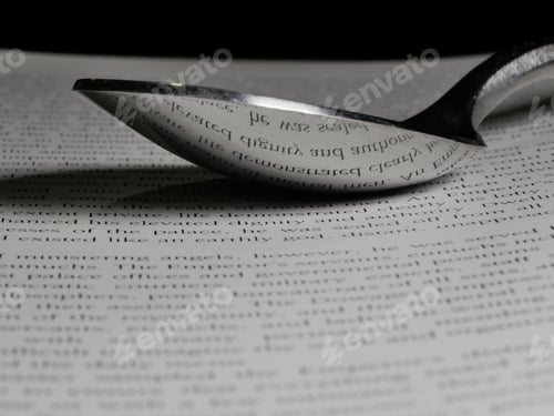 Preview: Closeup of an open book and a stainless steel spoon with the reflection of words