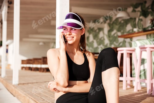 Preview: Young attractive sports woman talking on smartphone in cafe outdoors